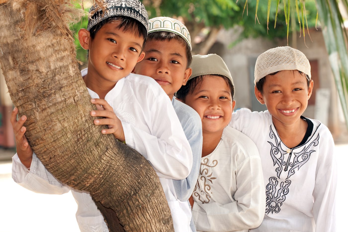 Four young children smiling together outdoors beside a tree